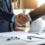 Businessmen shaking hands over blueprints in wpagain